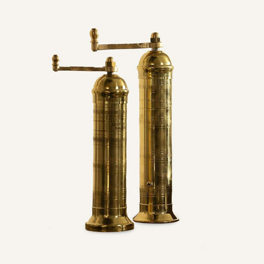 Two brass salt and pepper mills with hand-crank handles and engraved detailing, shown side by side at slightly different heights