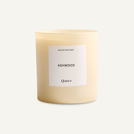Quince Ashwood candle in a cream glass vessel with a white label, viewed at a slight angle