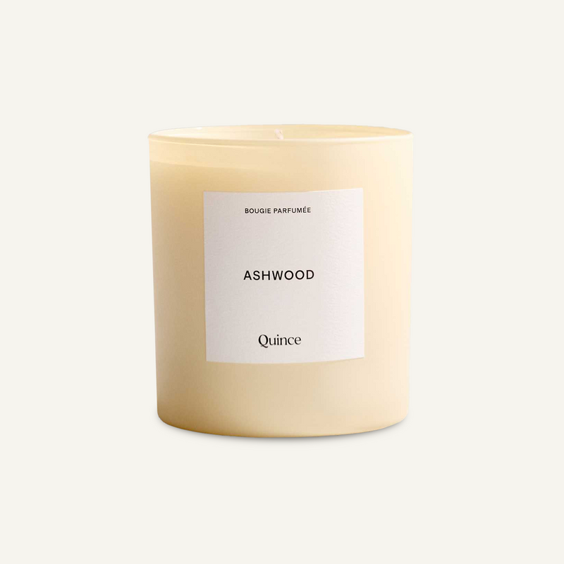 Quince Ashwood candle in a cream glass vessel with a white label, viewed at a slight angle